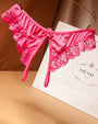 Pink lace crotchless thong with floral design, low waist, and Prada shopping bag background