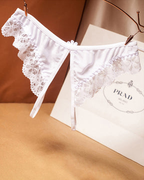 White lace crotchless thong with floral design, low waist, and Prada shopping bag background